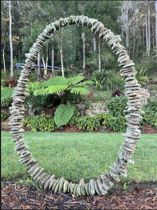 Stone circular arch sculpture framing tree ferns in the garden
